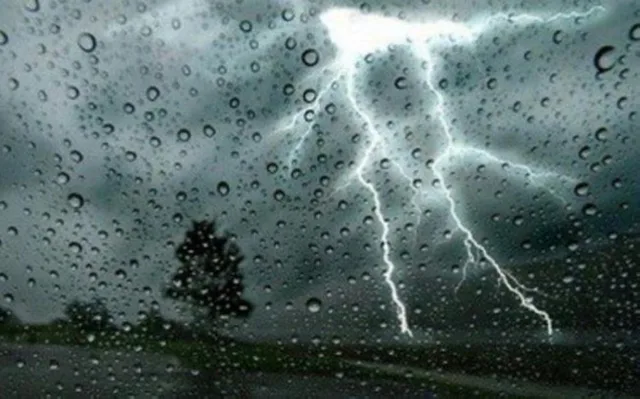 برق في سماء ملبدة بالغيوم خلف زجاج تغطيه قطرات المطر، صورة توضيحية