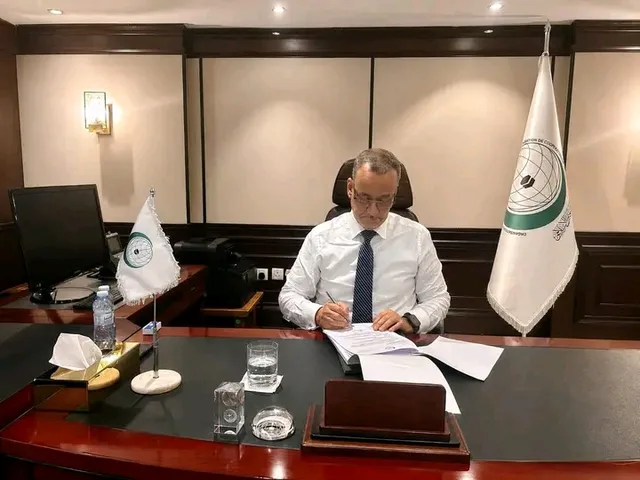 الأمين العام لمنظمة التعاون الإسلامي يوقع وثائق في مكتبه بجوار أعلام المنظمة
