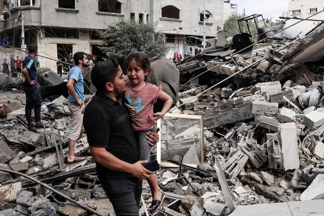 رجل يحمل طفلة تبكي وسط أنقاض مبنى مدمر في غزة، صورة أرشيفية من أكتوبر 2023