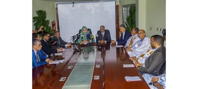 وزيرة التجارة والسياحة تتوسط مسؤولين إلى طاولة أمامها ميكروفونات