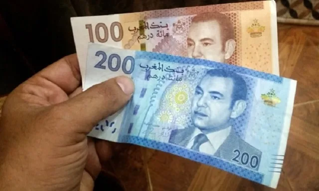 يد تمسك ورقتين نقديتين مغربيتين من فئة 100 و200 درهم، صورة أرشيفية