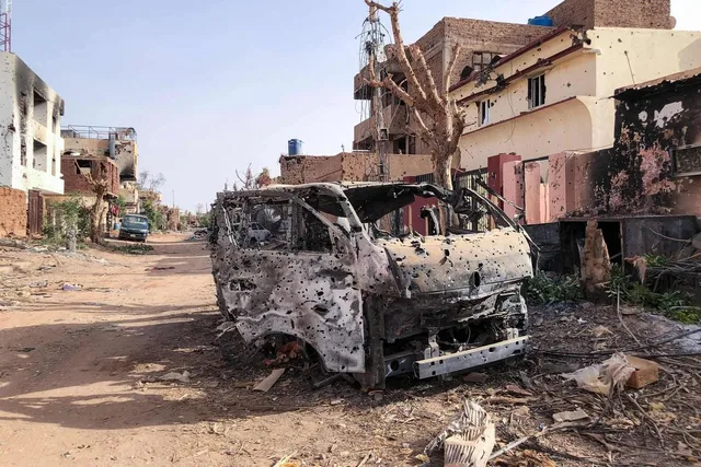 هيكل مركبة محترقة ومثقوبة بالرصاص في شارع متضرر بالحرب في السودان، صورة أرشيفية