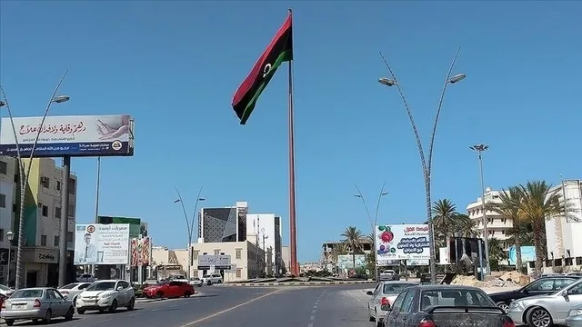 سارية عالية يرفرف عليها العلم الليبي وسط دوار تحيط به سيارات ومبان ولافتات، صورة أرشيفية