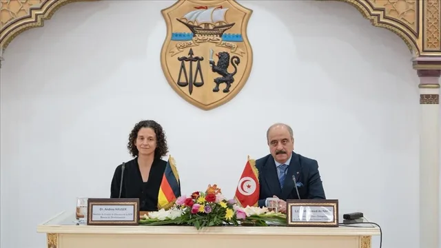 شعار الجمهورية التونسية معلق على جدار أبيض خلف طاولة رسمية عليها علما تونس وألمانيا، صورة أرشيفية